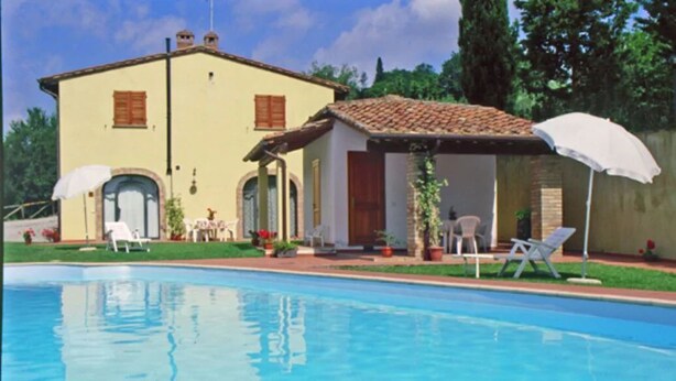 Un espace aménagé au bord de la piscine, comprenant une piscine, un bâtiment doté d’un toit en tuiles et du mobilier d’extérieur.