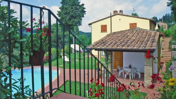 Ein Haus mit Ziegeldach, Swimmingpool und einem Garten mit roten Blüten.