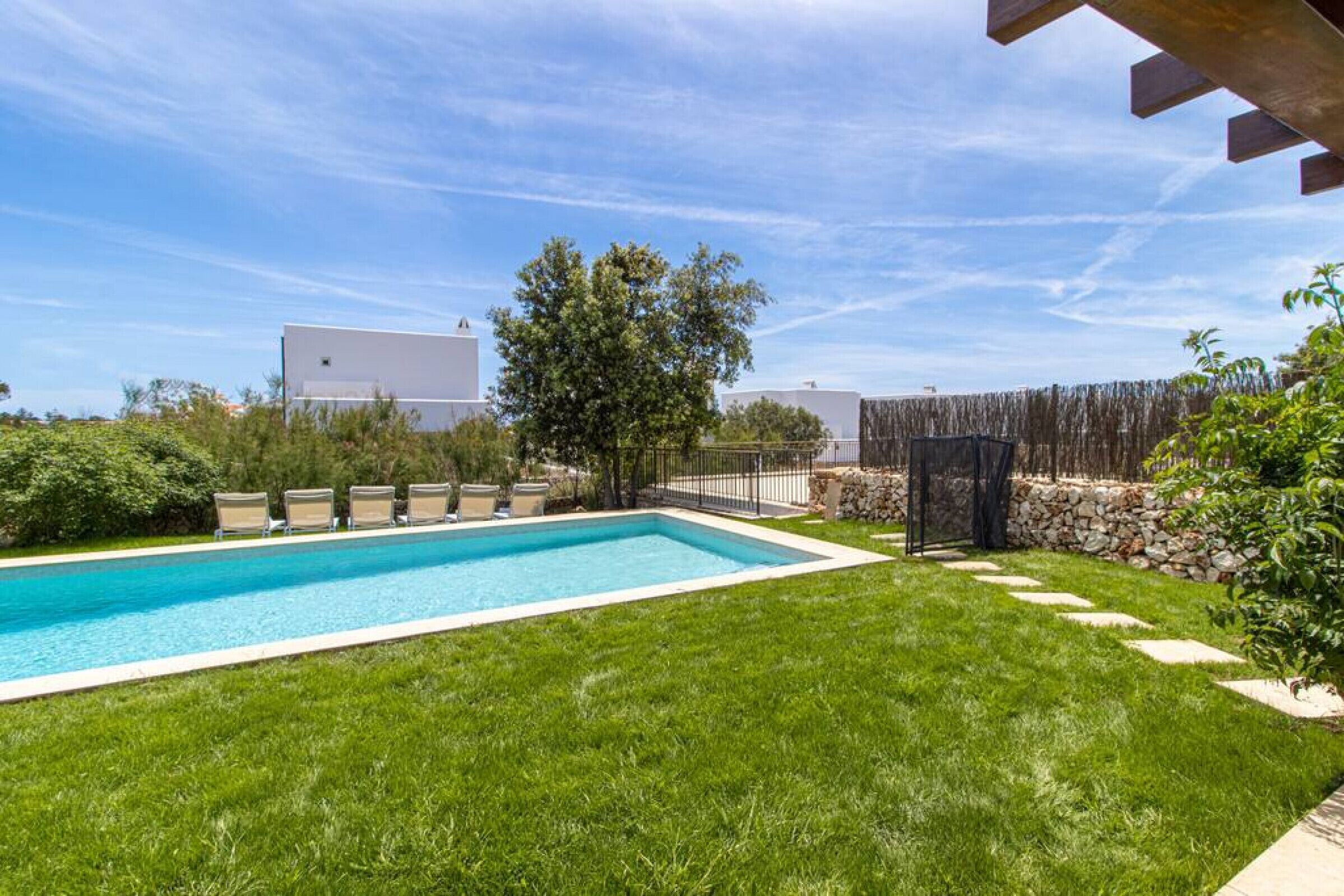 A rectangular swimming pool with a surrounding grassy area, a stone wall, and a wooden fence.