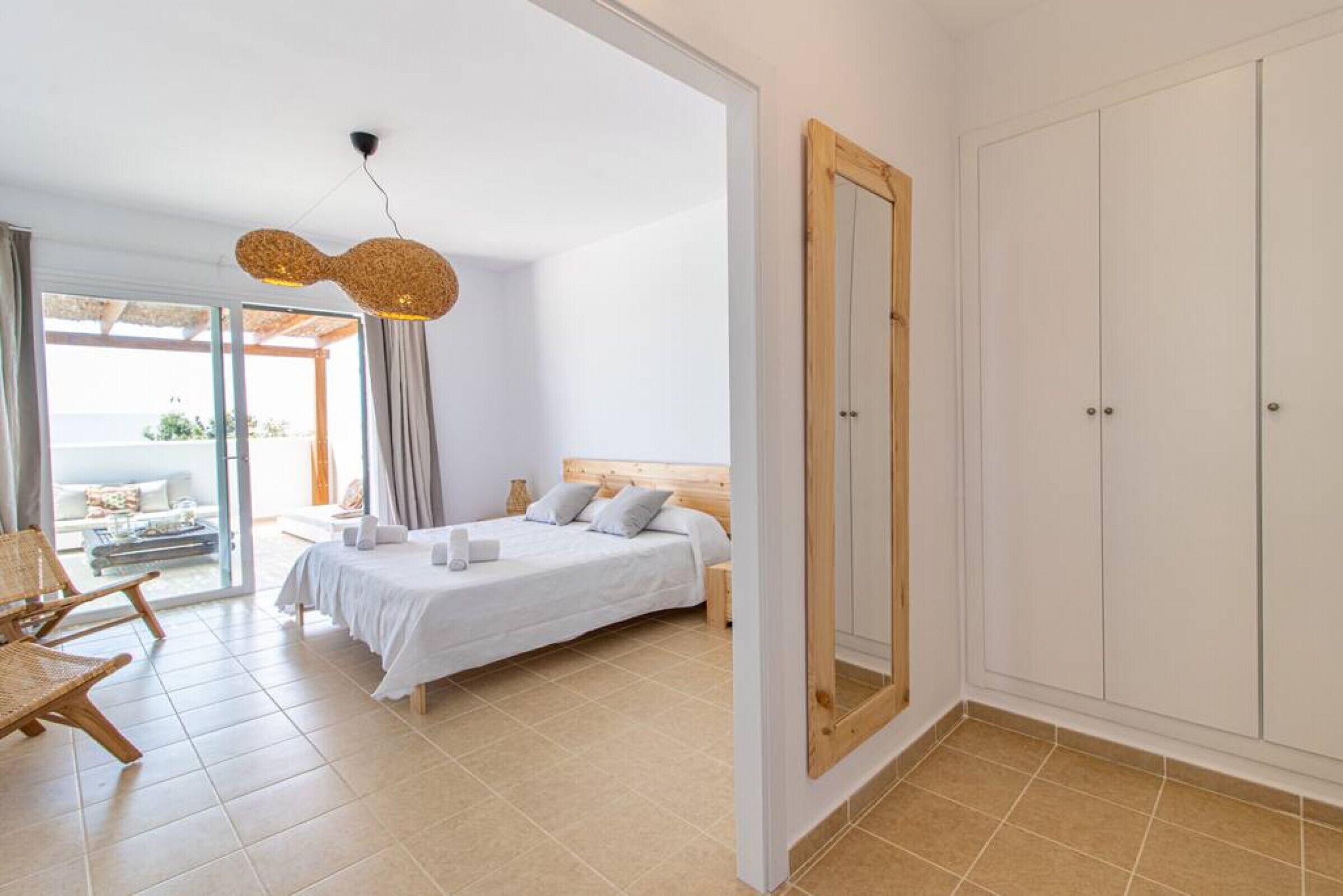 Ein Schlafzimmer mit Bett, Sessel, Kleiderschrank und großem Spiegel.