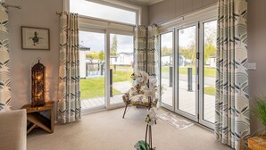A room with a large sliding glass door leading to an outdoor area, a patterned curtain, a framed picture, and a tall, ornate floor lamp. - Inside No. 1 Retreat (Carnforth)