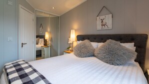 A bedroom with a large bed, two bedside lamps, a mirror, and a wall-mounted deer picture. - Inside No. 1 Retreat (Carnforth)