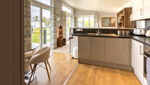 A modern kitchen with a central island, large windows, and a dining area with a glass table and chairs. - Inside No. 1 Retreat (Carnforth)