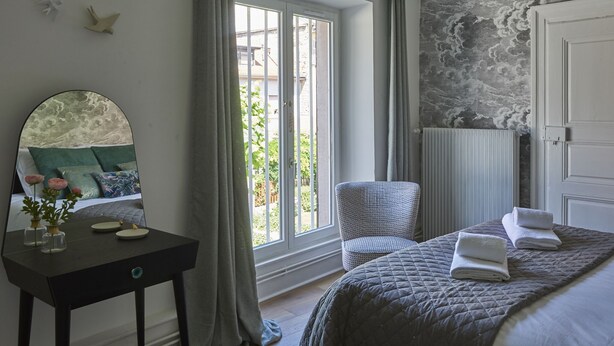 Un dormitorio con un ventanal grande, una silla, una mesita de noche y una cama con toallas.