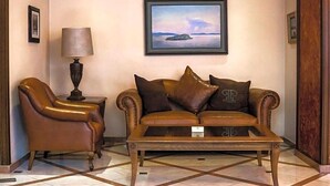 A lobby with a leather armchair, a sofa with brown cushions, a coffee table, and a framed picture of a landscape on the wall. - Park Hotel Volos (Volos)
