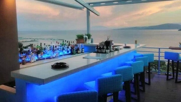 A bar with a view of the sea, bar stools, and a counter with bottles. - Park Hotel Volos (Volos)