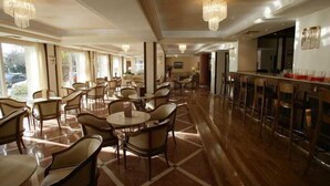 A spacious hotel lobby with multiple seating areas, a bar, and large windows allowing natural light. - Park Hotel Volos (Volos)