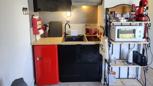A compact kitchen with a red refrigerator, a black dishwasher, a microwave, and a coffee maker on a shelf. - Bright studio in Pra-Loup with parking (Pra-Loup)