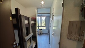 A narrow hallway with bunk beds on the left, a radiator on the right, and a window at the end. - Bright studio in Pra-Loup with parking (Pra-Loup)