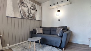 A modern living room with a grey sofa, a small round table, a fluffy rug, a wall-mounted shelf with decorative items, and a large abstract painting. - Bright studio in Pra-Loup with parking (Pra-Loup)