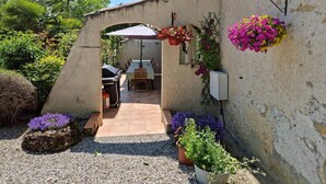Un espace extérieur aménagé en terrasse, avec une table et des chaises, entouré de plantes en pot et de suspensions florales.