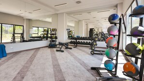 Un gimnasio con equipo de ejercicio diverso, espejos y ventanas.