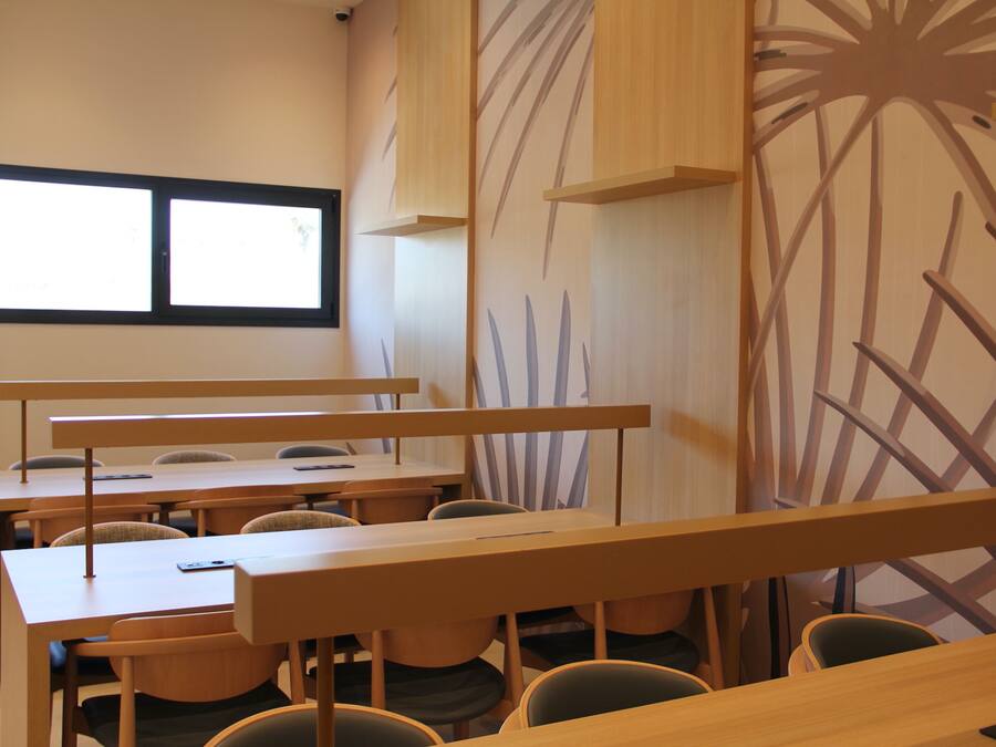 A classroom with wooden desks and chairs, a large window, and a wall with a plant design.