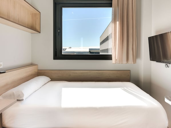 Quarto de hotel com cama, televisão, janela com cortinas e vista para prédios.