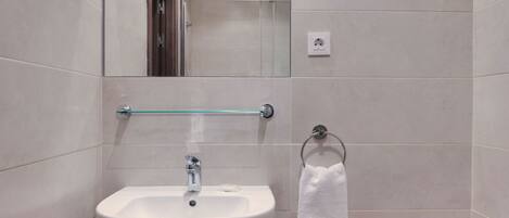 A bathroom with a white sink, a glass towel rack, and a mirror.