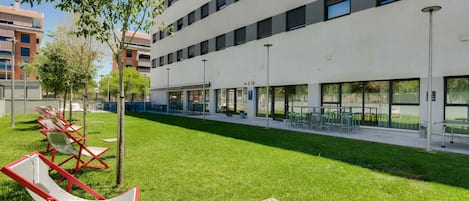 A modern building with a flat roof, large windows, and a grassy courtyard with outdoor seating.