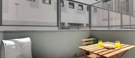 A balcony with a table, chairs, and a view of a building with multiple windows.