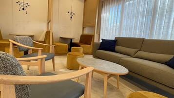 Un salon moderne avec un canapé, des fauteuils, une table basse et une grande fenêtre agrémentée de rideaux.