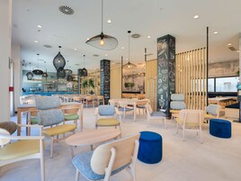 Interior de una cafetería moderna con mesas y sillas de madera, lámparas colgantes y una pared con menú en la pizarra.