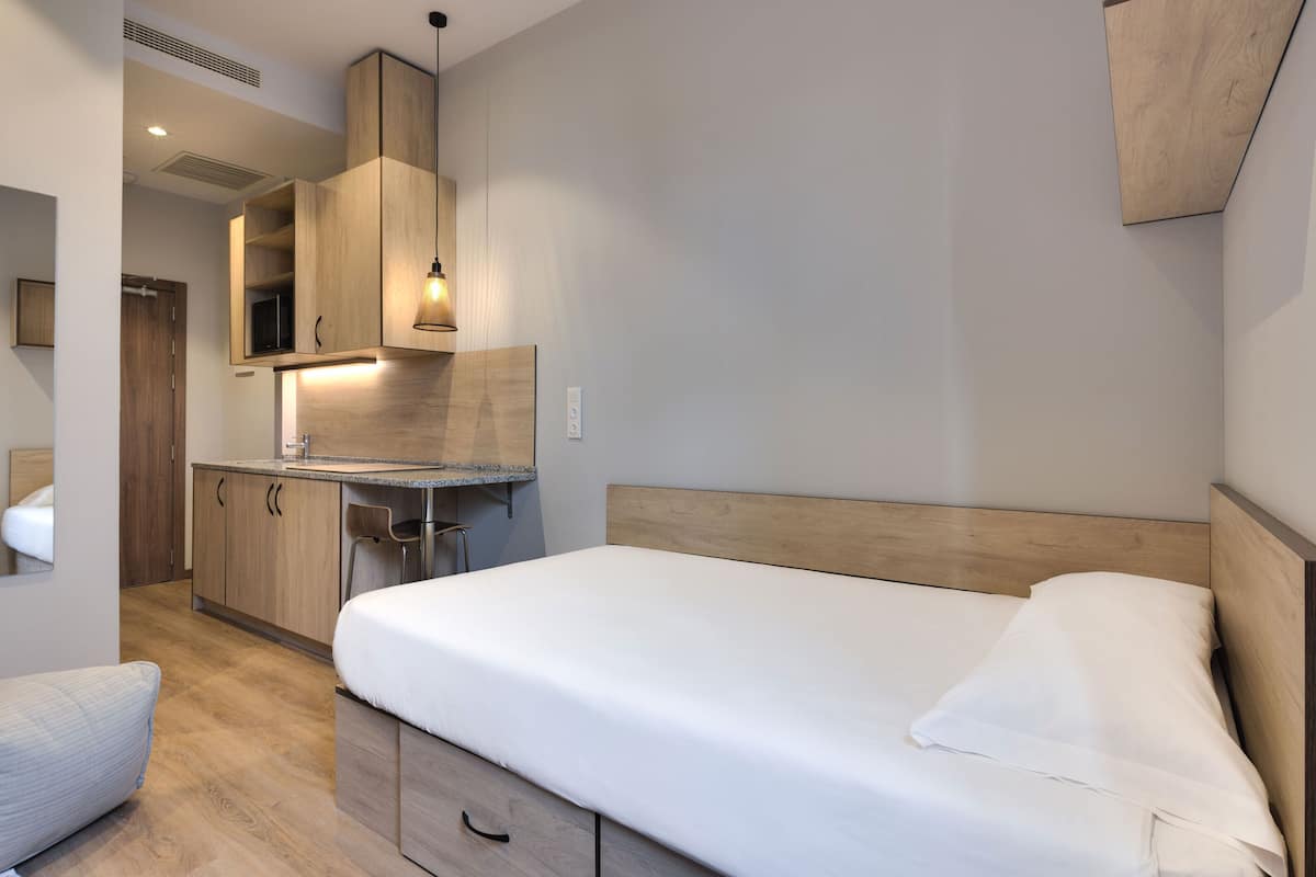 Ein kleines Hotelzimmer mit Bett, einer kleinen Küchenzeile und einem Holz-Kopfteil.