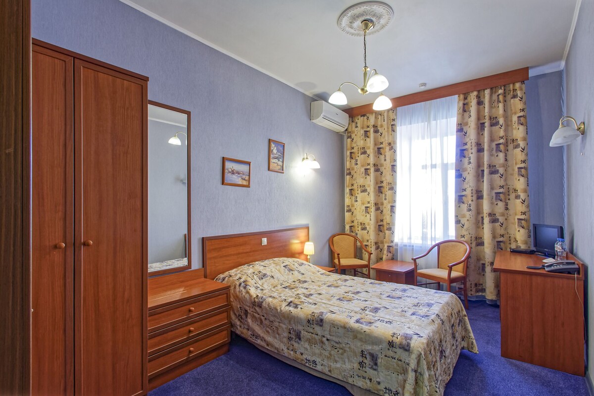A hotel room with a bed, wooden wardrobe, desk, chair, and a television.