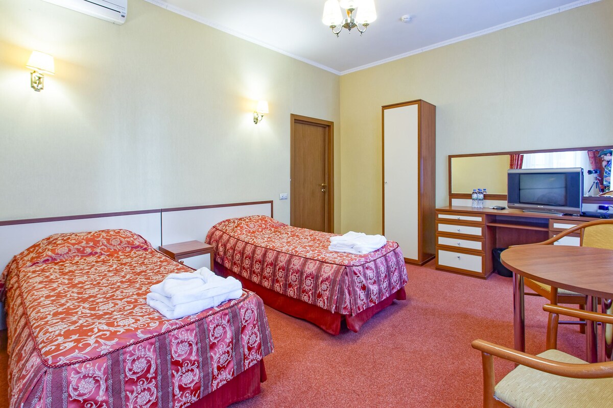 A hotel room with two beds, a desk, a chair, a television, and a mirror.