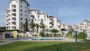 A modern apartment building with a swimming pool, surrounded by well-maintained lawns and palm trees. - Vilamoura House Garden by Hopstays | Marina view (Vilamoura)