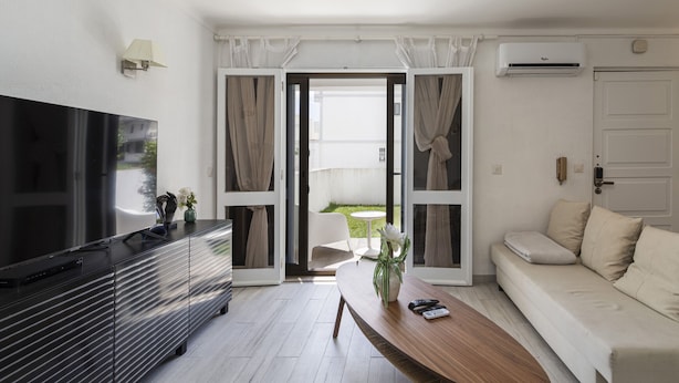 A modern living room with a flat-screen TV, a wooden coffee table, a sofa, and a sliding glass door leading to a balcony. - Vilamoura House Garden by Hopstays | Marina view (Vilamoura)