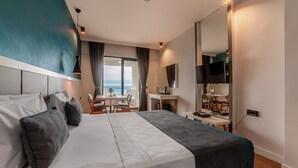 Habitación de hotel moderna con una cama grande, un escritorio, un televisor y vista al mar.