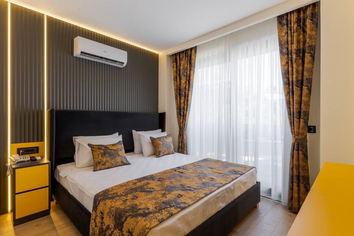 A modern hotel room with a large bed, a bedside table with a phone, and an air conditioning unit on the wall.
