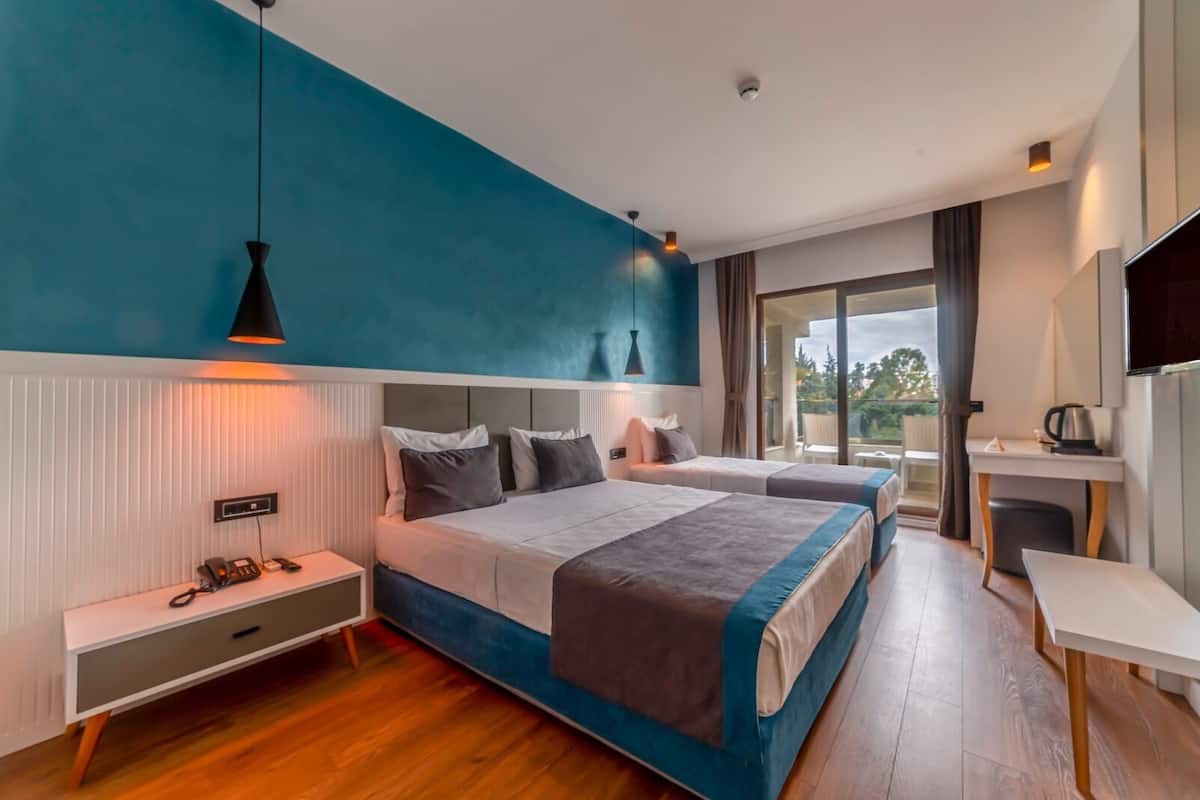 A modern hotel room with a large bed, bedside tables, a desk, and a balcony with a view.