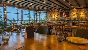 Un restaurante con mesas y sillas de madera, un muro de ladrillo con detalles decorativos y ventanas amplias que dejan entrar luz natural.