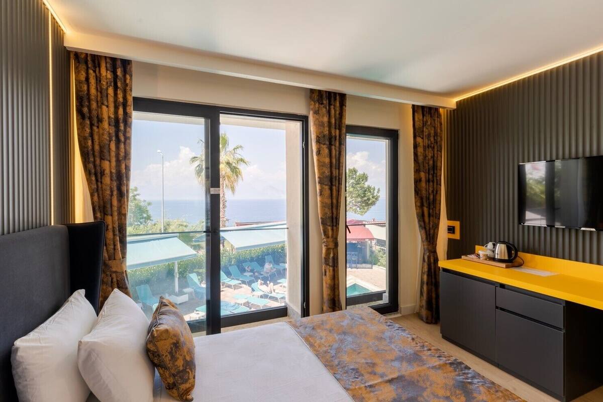 A hotel room with a bed, a TV, a yellow counter, and a view of the sea.