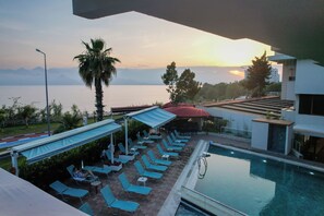 A pool area with lounge chairs and umbrellas, overlooking a body of water and mountains. - Tema 242 Hotel (Antalya)