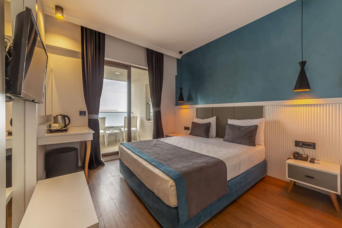 A modern hotel room with a large bed, bedside tables, a desk, and a view of the outside.