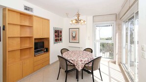 A dining area with a table and chairs, a wooden cabinet with a television, and a window with a view.