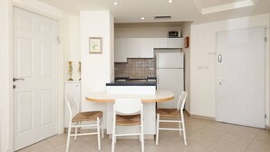 A compact kitchen with white cabinets, a white refrigerator, and a small dining area with a round table and two chairs.