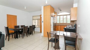 A dining area with a table and chairs, a kitchen with cabinets and a stove, and a window providing natural light. - Keren Kayemet - Four Bedroom Apartment, Sleeps 8 (Jerusalem)