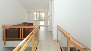 A spacious hallway with a wooden bench and glass railings, leading to a balcony with a view of greenery. - Keren Kayemet - Four Bedroom Apartment, Sleeps 8 (Jerusalem)