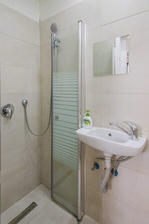 Et badeværelse med brusekabine i glas, vask med spejl og en shampoo-flaske.