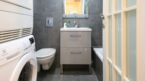 A compact bathroom with a washing machine, toilet, and a sink with a mirror above. - King David Elegance - Two Bedroom Apartment, Sleeps 4 (Jerusalem)
