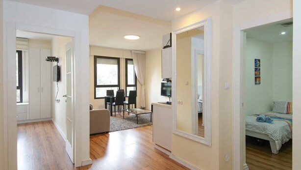 A spacious living area with a dining table, chairs, a TV, and a bed with a striped blanket. - King David Elegance - Two Bedroom Apartment, Sleeps 4 (Jerusalem)