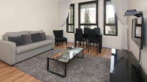 A modern living room with a grey sofa, black chairs, a glass coffee table, and a flat-screen TV. - King David Elegance - Two Bedroom Apartment, Sleeps 4 (Jerusalem)