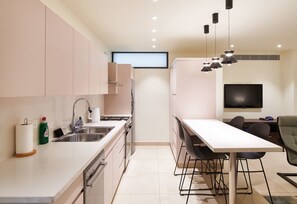 A modern kitchen with a dining area, stainless steel appliances, and a flat-screen TV.