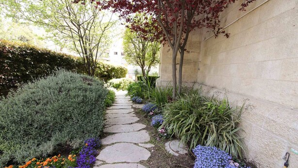 Un chemin de pierres bordé de différentes plantes et fleurs, menant à un bâtiment doté d’un mur en pierre.
