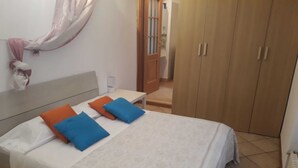 Un dormitorio con cama, almohadas, mesita de noche, armario y baño a la vista.