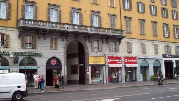 Un edificio amarillo con varias fachadas comerciales, incluyendo una farmacia y una tienda Vodafone.