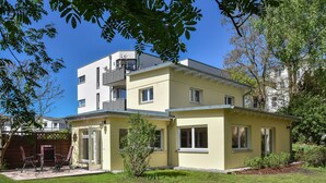 Un bâtiment à deux étages, doté d’un toit plat, d’un balcon et d’une petite structure adjacente avec une porte et des fenêtres.