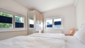 Une chambre avec deux lits, une armoire et deux fenêtres équipées de stores.