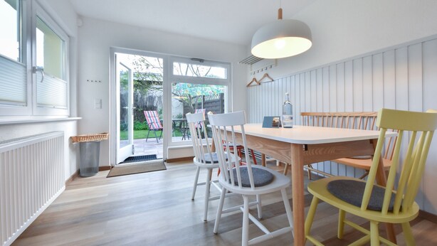 Un coin repas avec une table et des chaises en bois, un luminaire suspendu et une vue sur un jardin extérieur, accessible par une porte vitrée.